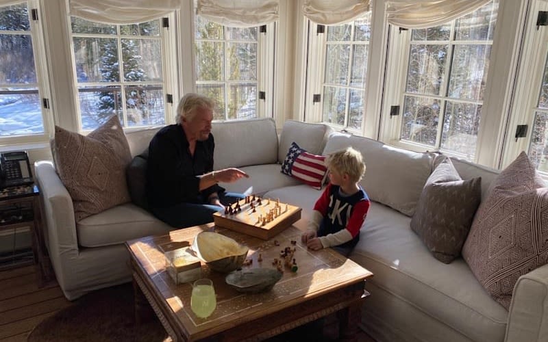 Richard Branson sitting on a sofa playing chess with his young grandson 