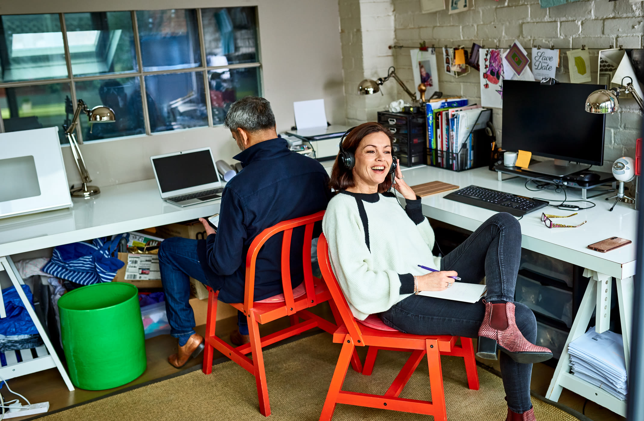 A woman on the phone in a home office with a man behind her on a tablet