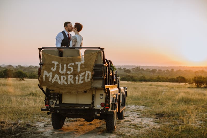 A couple kiss in a safari jeep with a Just Married sign on the back of it