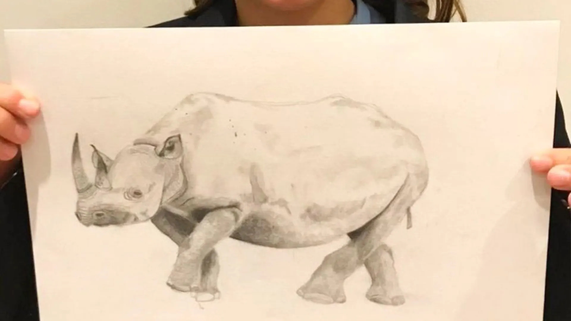 A child holds up a drawing of a rhino they have produced