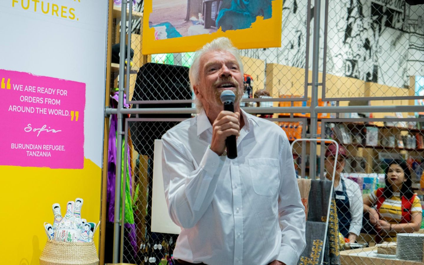 Richard Branson in white shirt holding a microphone and smiling