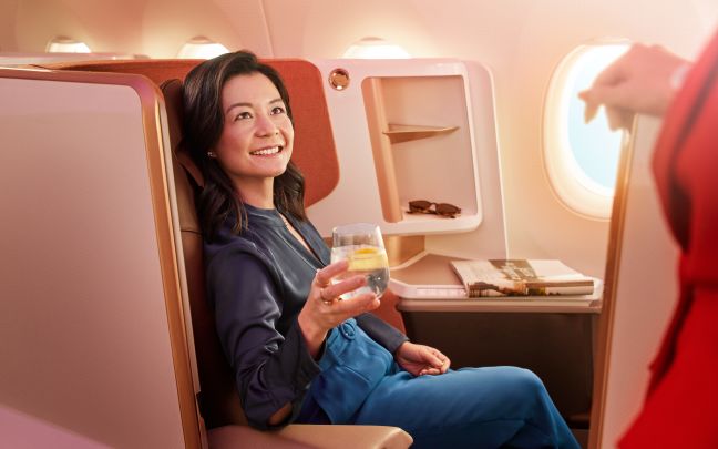 Image of a lady with a drink sat in Upper Class, smiling at a member of cabin crew.