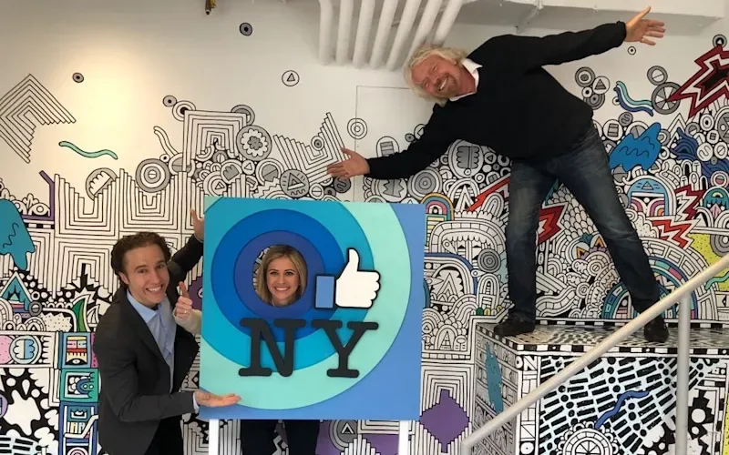 Holly Branson, Richard Branson and Craig Kielburger pose for a photo. Holly has placed her head in a frame that has blue circles, the Facebook 'like' symbol and 'NY' written on it.