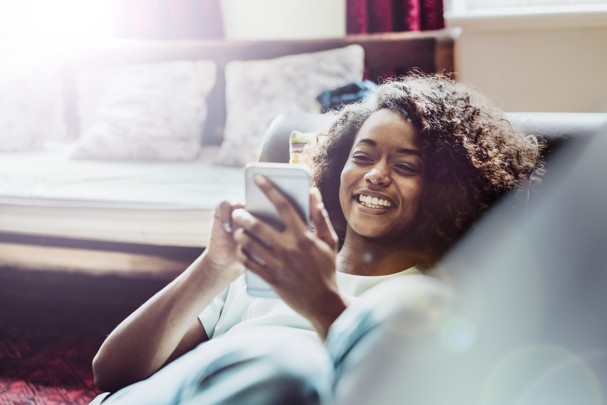 A smiling woman looking at her phone while lying on a sofa