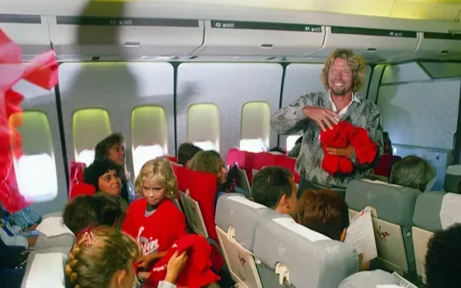 Richard Branson hands out red Virgin shirts on an early Virgin Atlantic flight with his daughter Holly