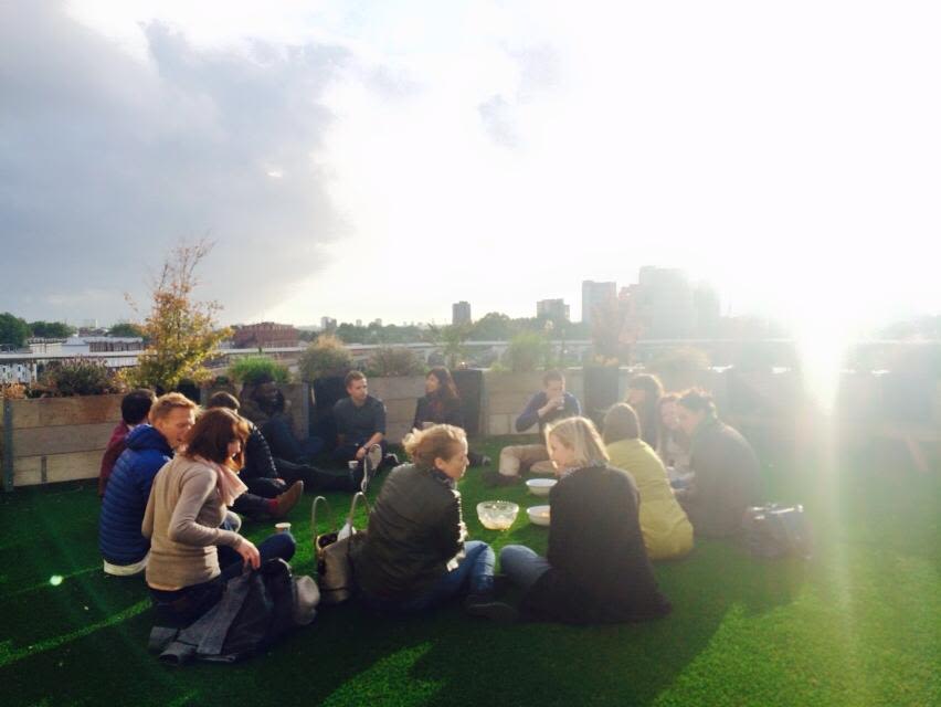 A group of people sit on a rooftop drinking and discussing books