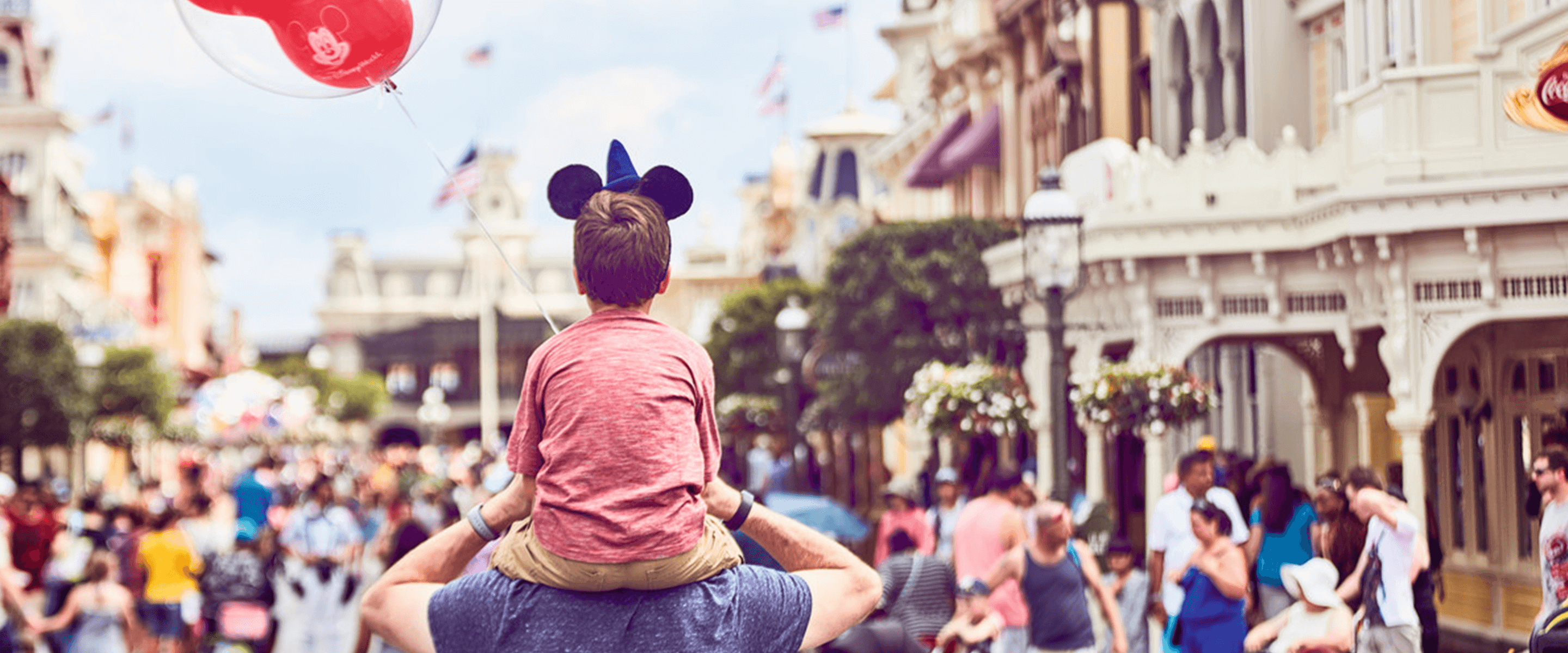 A child sitting on their parent's shoulders wearing Mickey Mouse ears at Walt Disney World Florida