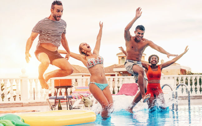 Image of four happy friends drinking jumping in pool sunset party.