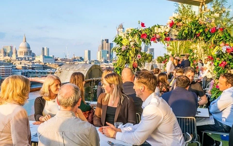 Image of a busy rooftop terrace at the OXO Brasserie with a flower arch and distant view of St Paul's Cathedral.