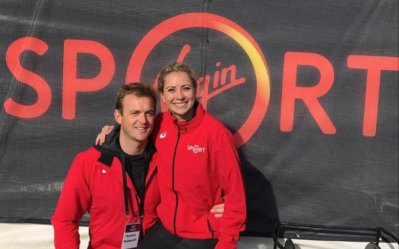 Holly Branson and Freddie Andrewes in front of a sign with the Virgin Sport logo on it