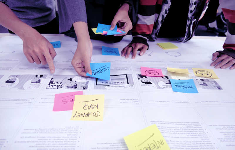 hands adding sticky notes on a journey map illustration