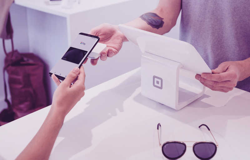 Image showing two people at a checkout desk. One person uses their phone to pay with a digital credit card.