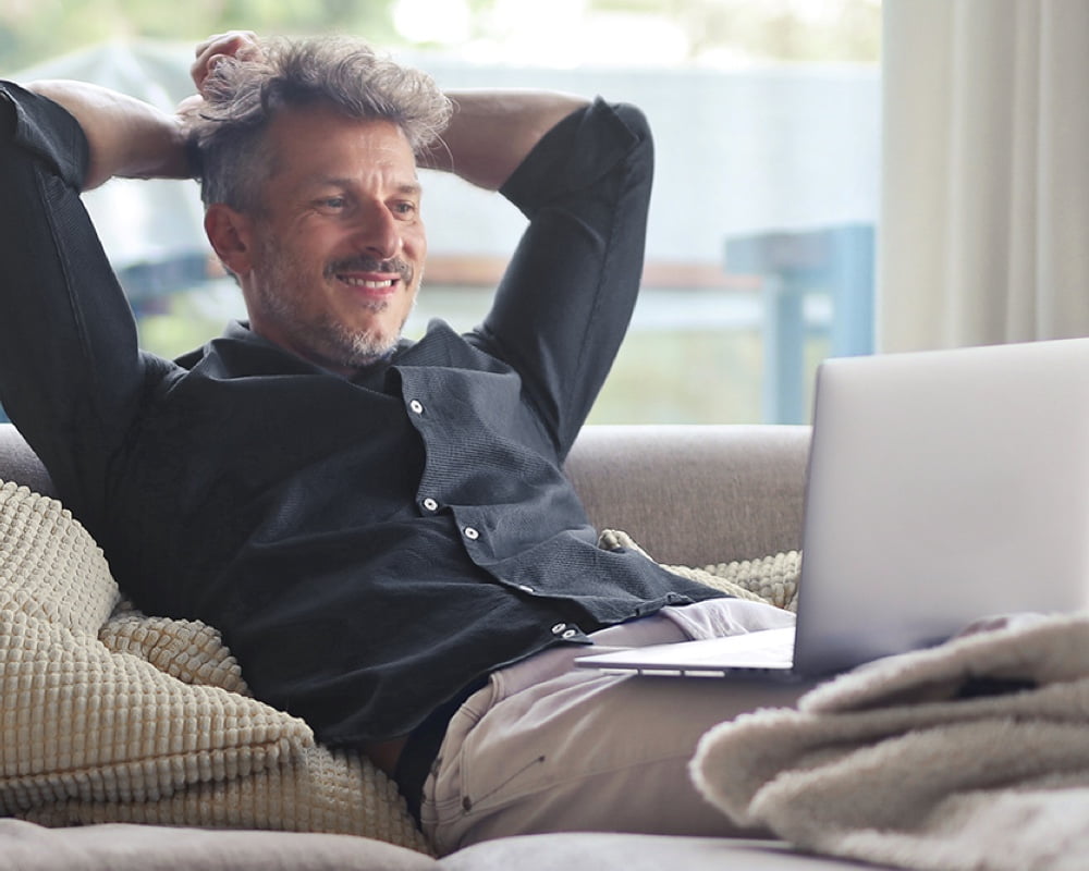 Man leaning back on his couch, looking at his laptop