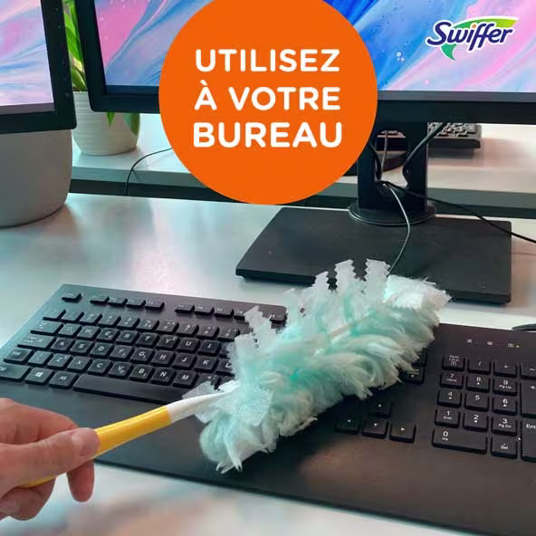 Swiffer duster utilisé pour nettoyer un clavier sur un bureau avec deux écrans dans un environnement de bureau propre.