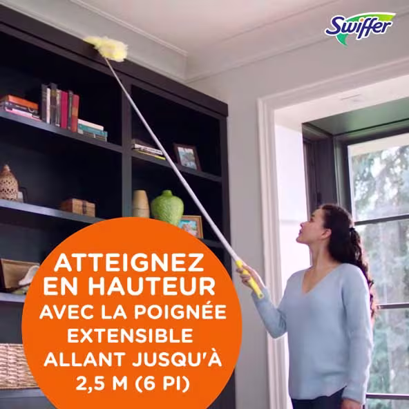 Femme utilisant une balayette Swiffer avec un manche extensible de 6 pieds pour nettoyer les étagères en hauteur dans un salon lumineux.