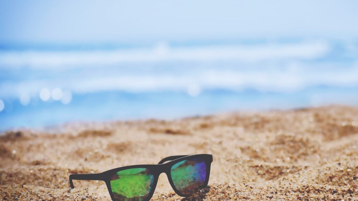Sunglasses sat in the sand on a beach