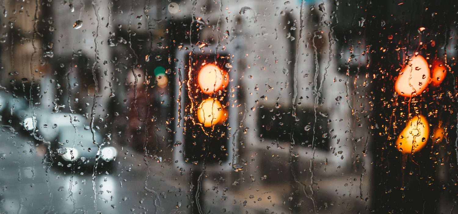Raindrops on a window with blurred traffic lights in the background.