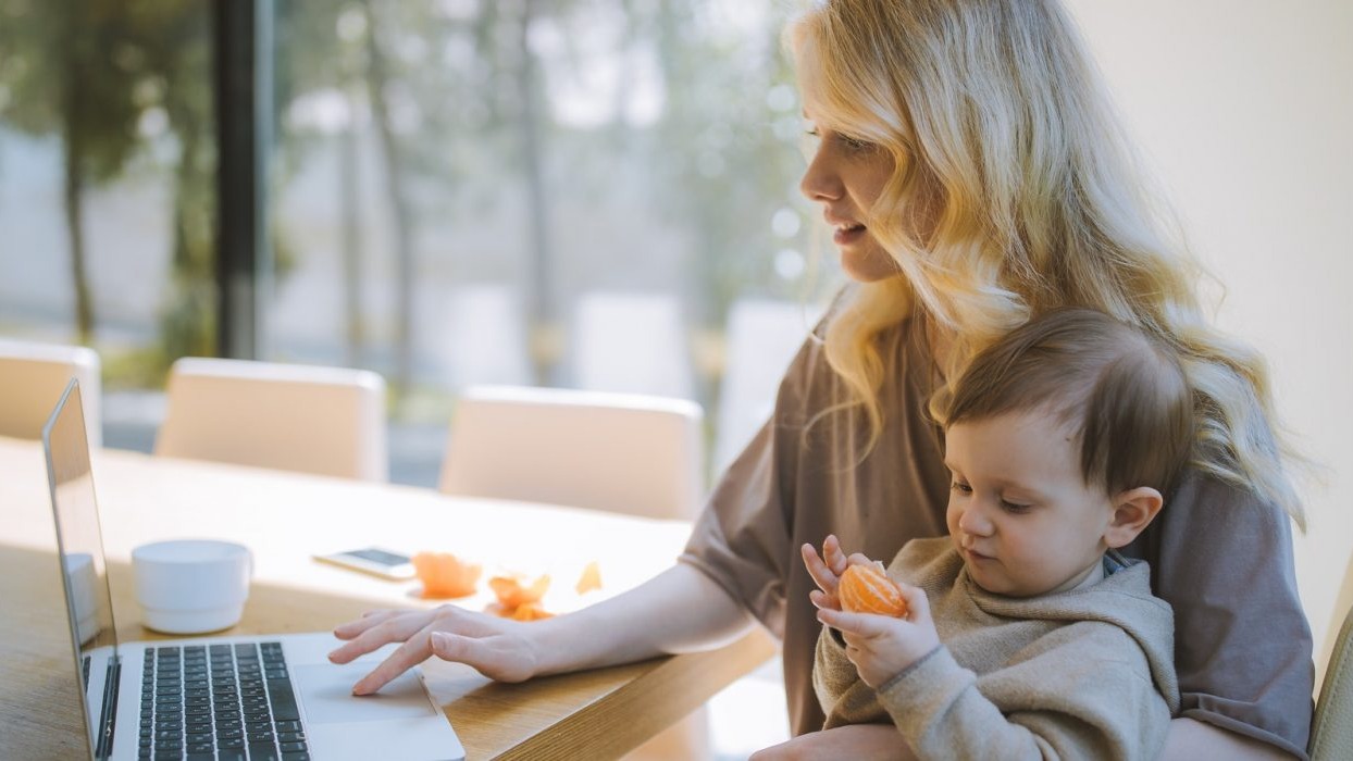 Mother holding child whilst working on a laptop