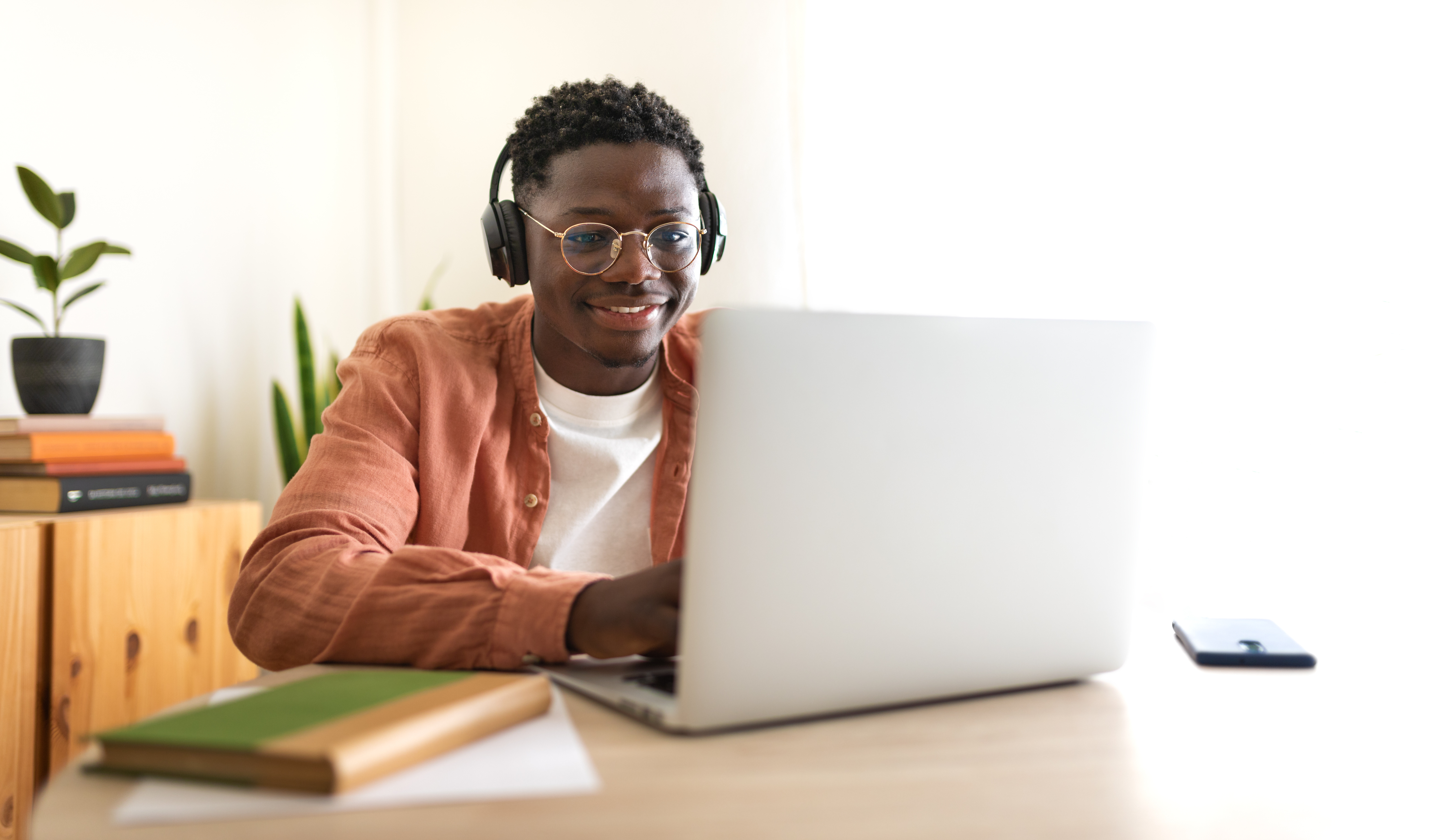 Student wearing headphones, smiling, and working on a laptop