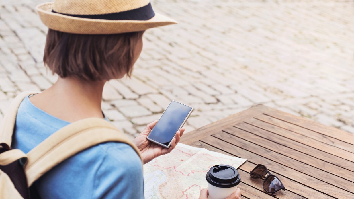 Person sat at a table holding a mobile phone and coffee 