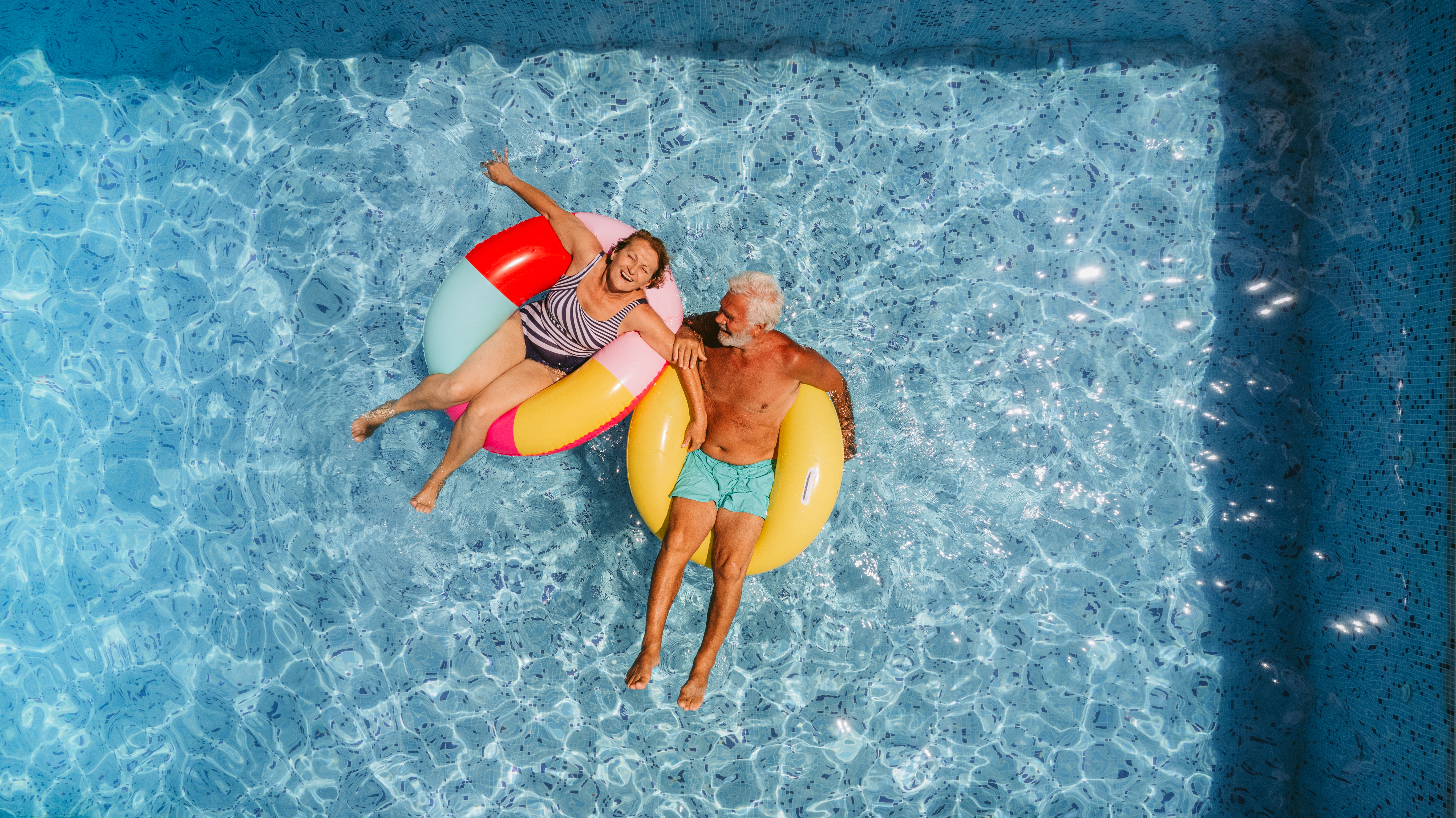 A couple floating in swimming pool on inflatable rings.