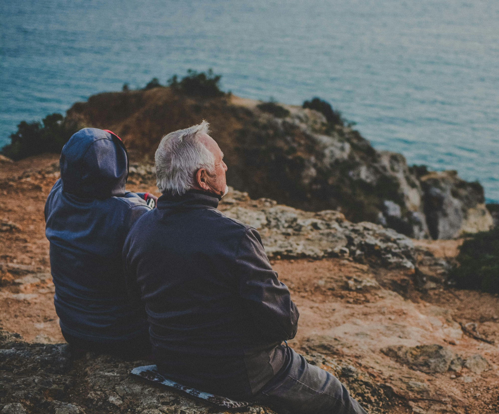older couple sitting on a rock looking out to sea
