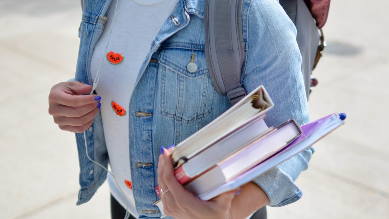 Person in denim jacket holding books 