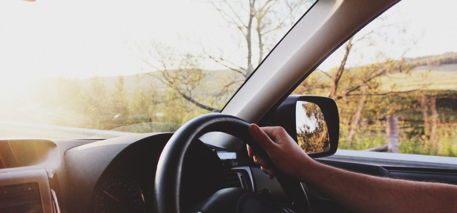 Driver's view inside a car, showing a hand on the steering wheel