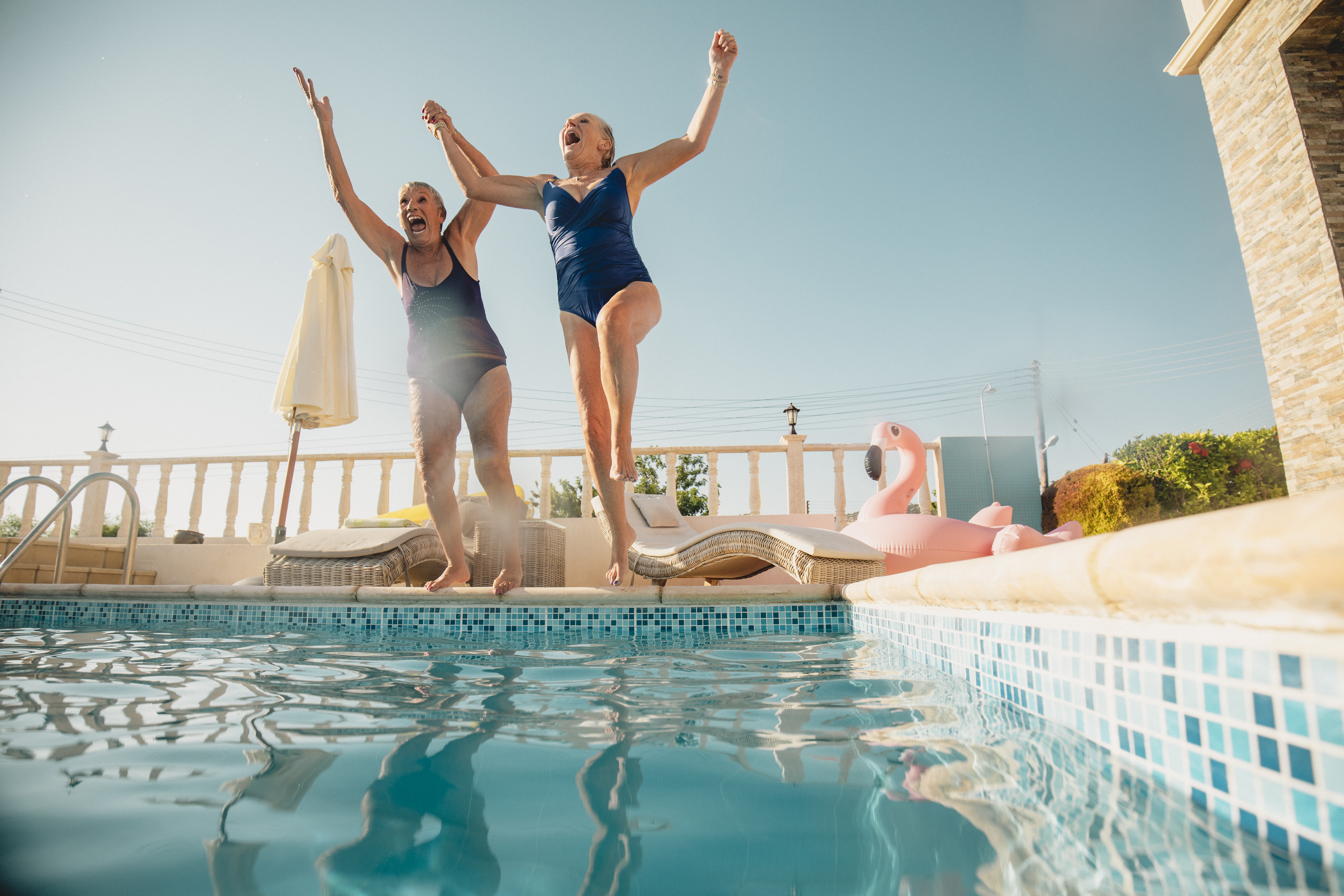 Two women jumping into a swimming pool on holiday