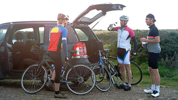 Three male cyclists stood next to an SUV with the car boot open.