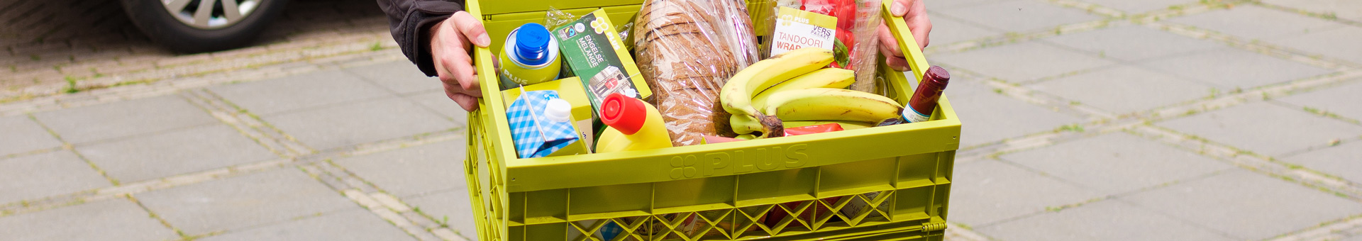 PLUS-krat met boodschappen zoals brood, bananen, wijn, sap en melk.