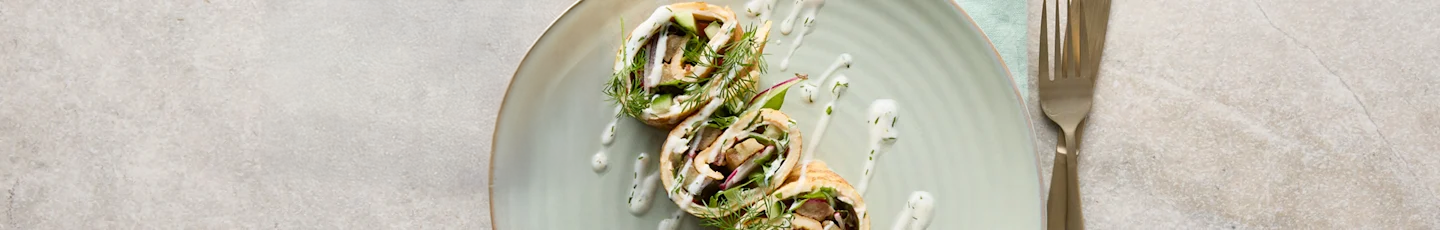 Gezond tussendoortje: wraps gevuld met groenten, gegarneerd met verse dille en besprenkeld met een witte dressing.