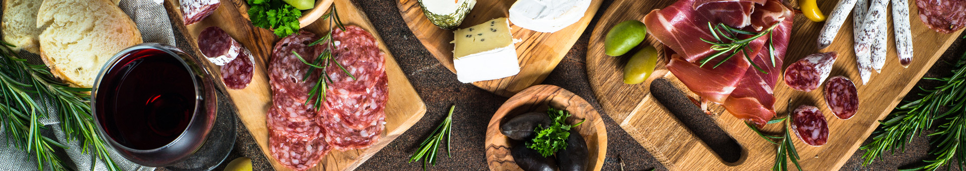 Borrelplank met salami, prosciutto, diverse kazen, olijven, brood en een glas rode wijn.