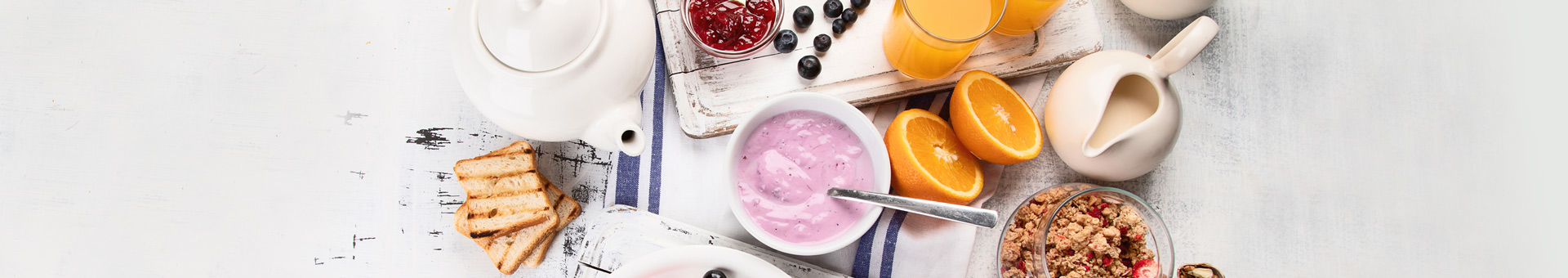 Ontbijttafel met roze yoghurt, sinaasappels, toast, granola, jam, blauwe bessen, sinaasappelsap.