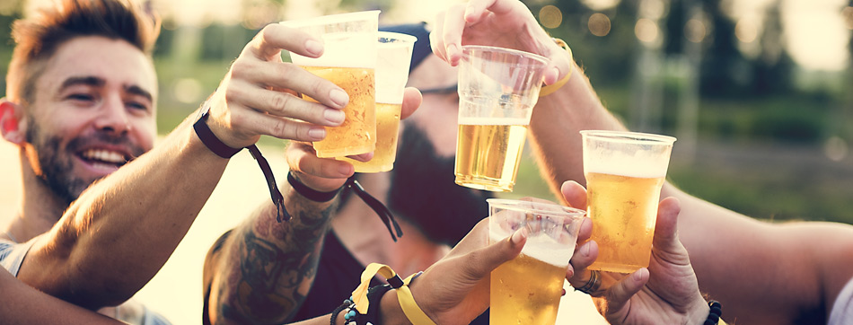 Groep mensen proost met plastic bekers bier tijdens een buitenevenement.
