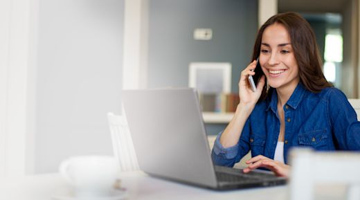 A white woman talks on her phone while sitting in front of her laptop computer