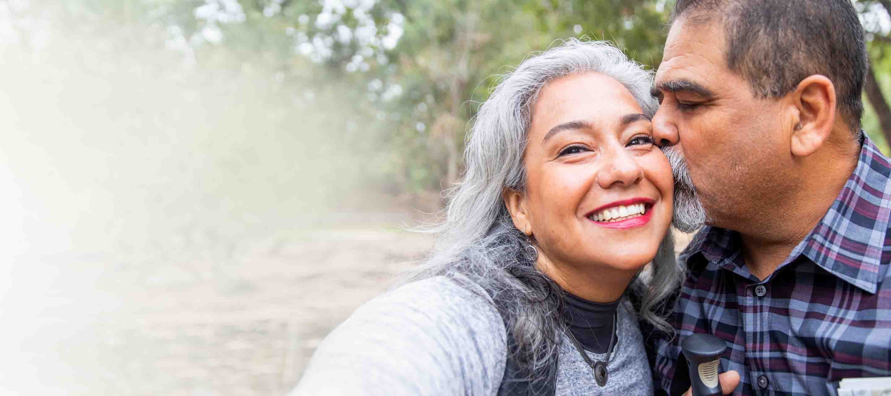 An older Hispanic couple stops for a selfie and a kiss on a nature hike
