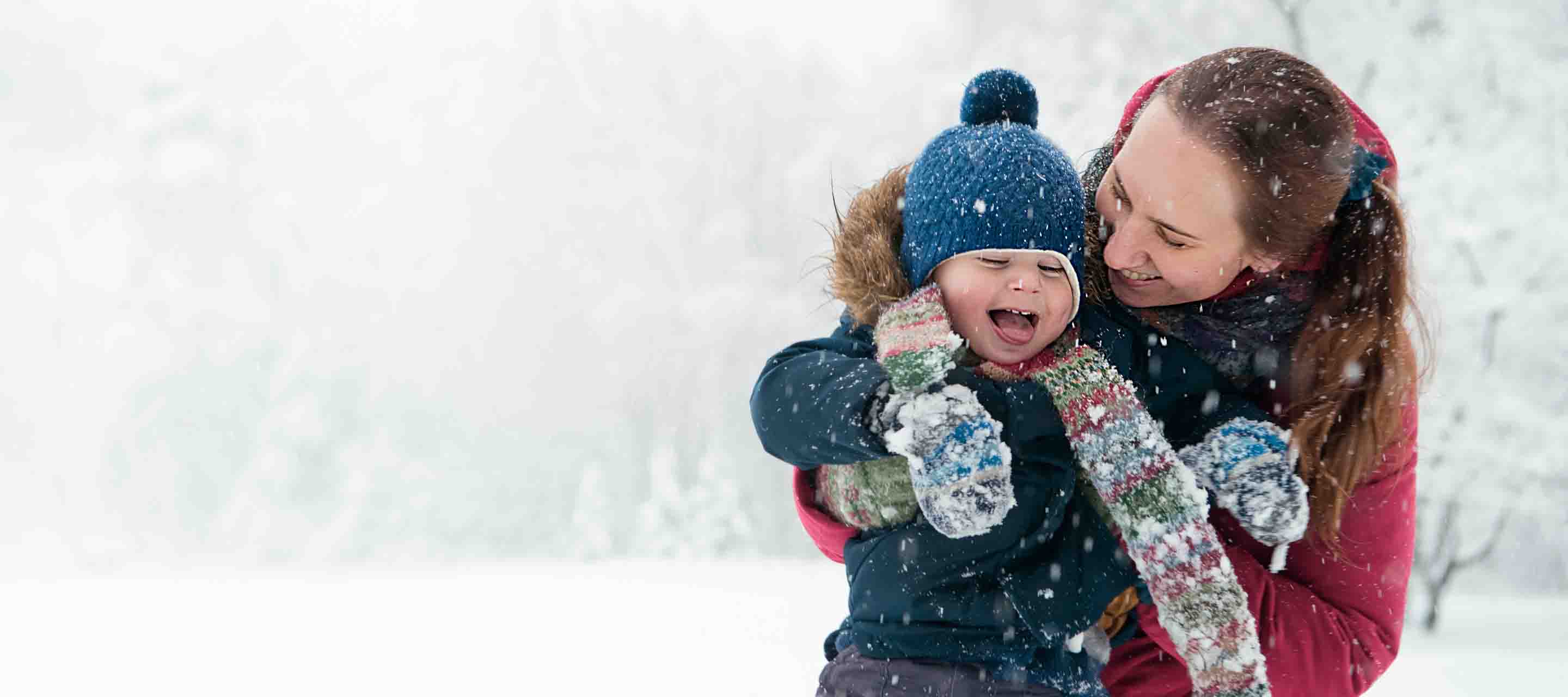 A happy child gets help from his mother as he tries to catch snowflakes on his tongue at a park in the winter