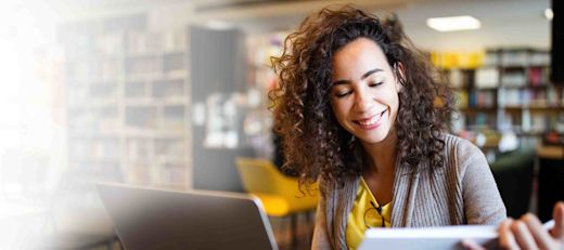 A female entrepreneur looks over a binder and laptop in a library.
