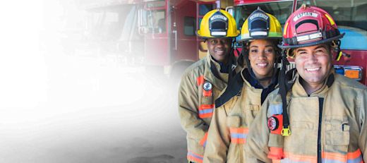 Three smiling firefighters standing in front of fire trucks.