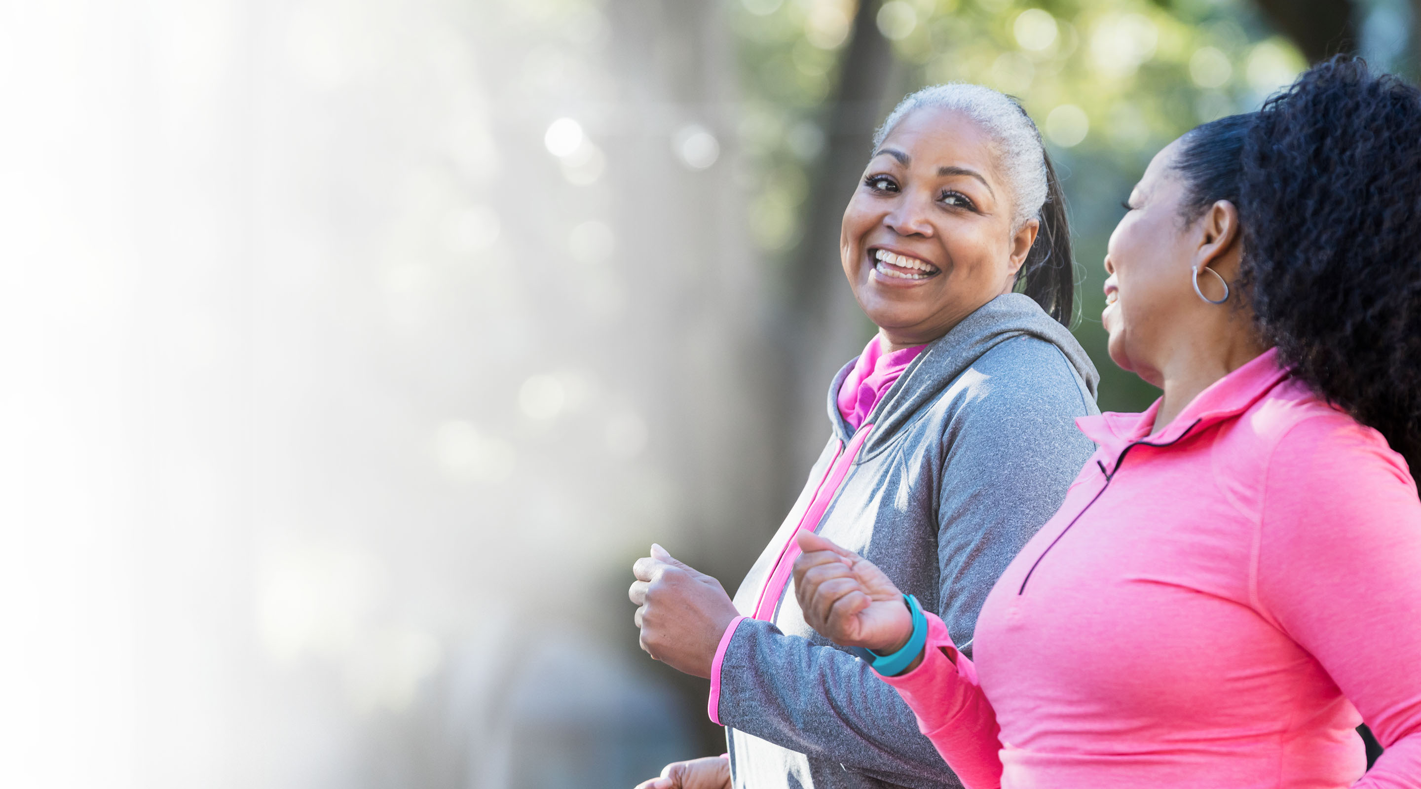 Two Black women exercise together by taking a brisk walk in the park