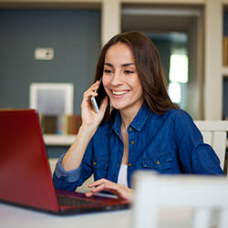 Female sales rep talking on the phone while working on a laptop.