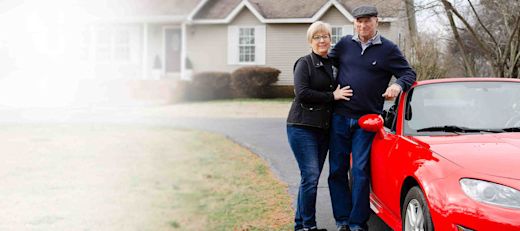 A couple stands beside their red sports car