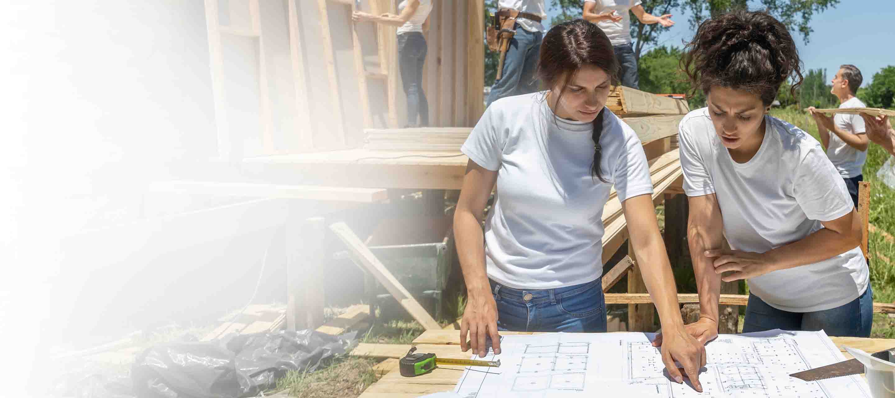 Two female construction workers discuss blueprints for a community building project
