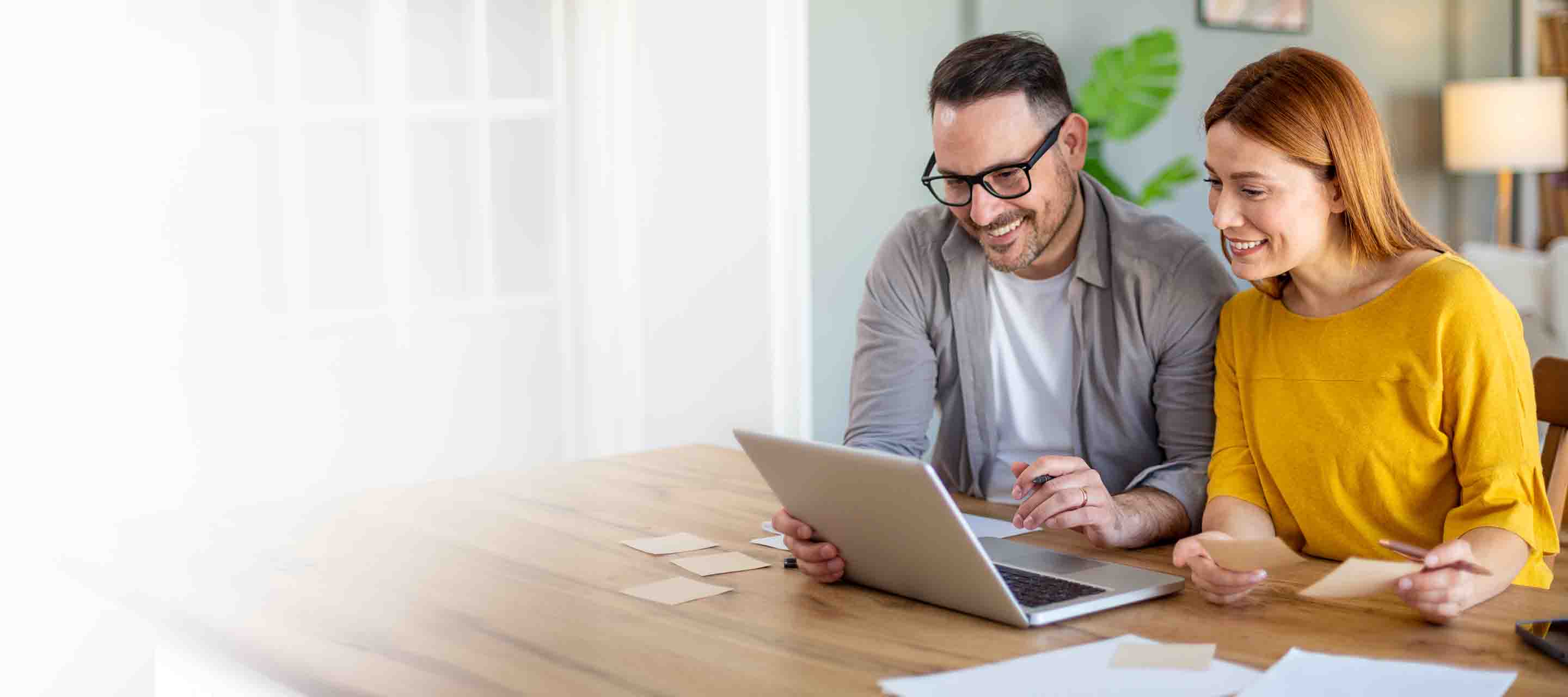 Happy smiling couple sitting together at home table with laptop.