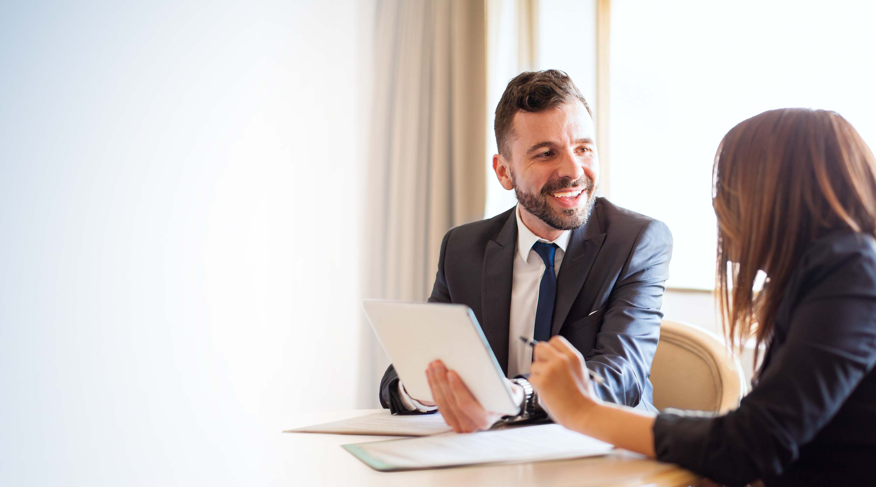 A suited white man discusses paperwork with a white female