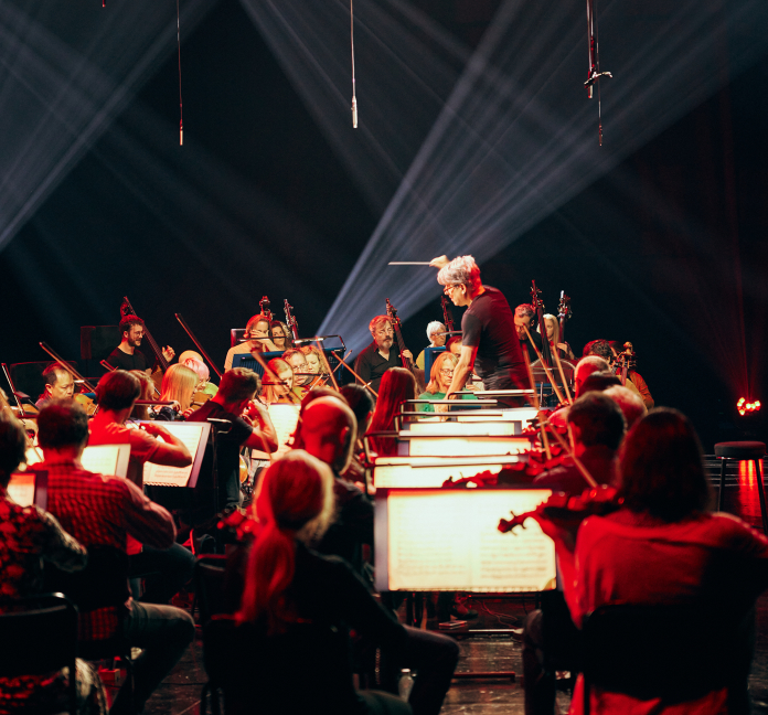 Conductor Peter Breiner leading the Royal Philharmonic Orchestra at the recording of the global livestream performances of Igor Stravinsky's 'The Firebird', 'Petrushka', and 'The Rite Of Spring' under red stage lighting