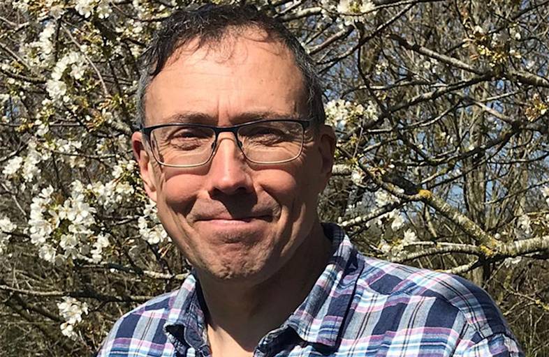 A man wearing glasses in a checked shirt smiling.