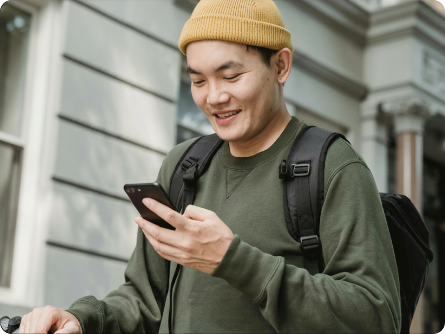 Smiling man in a yellow beanie and backpack using his phone on a city street to book travel with Zip buy now, pay later