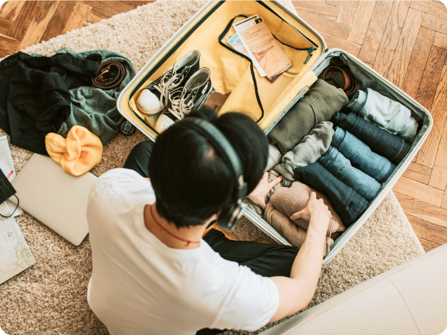 Person in headphones packing a suitcase with folded clothes and sneakers for a trip booked with Zip buy now, pay later